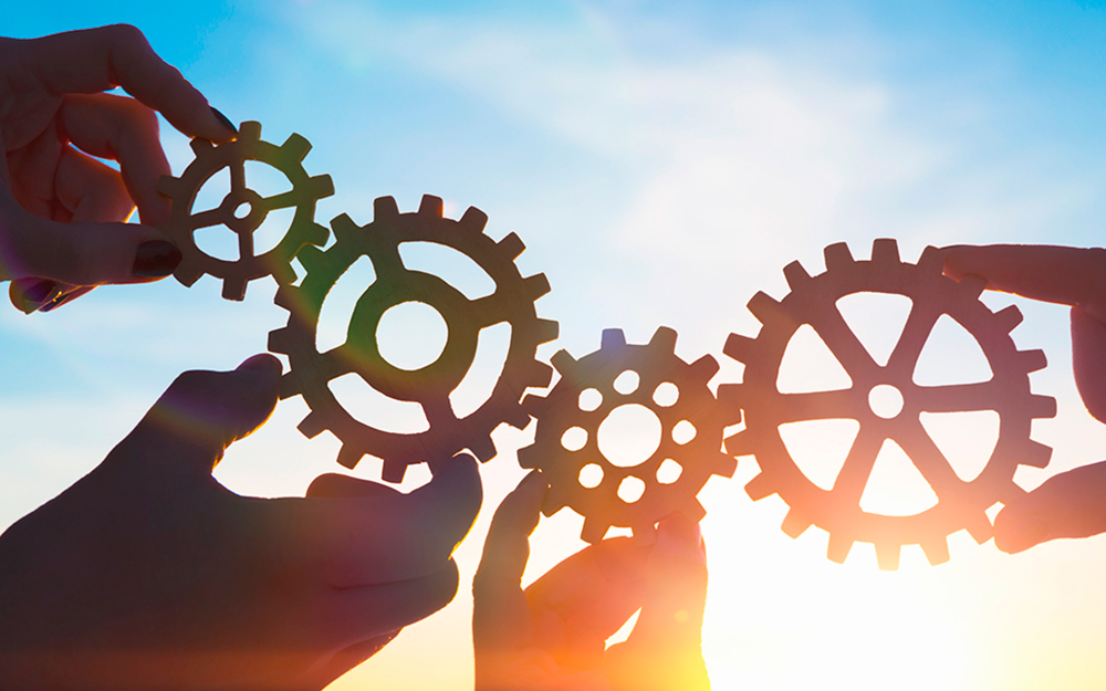 Hands holding interconnected gears against a sky background, symbolizing collaboration and teamwork.